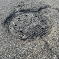 asphalt showing what a manhole collar that might need repair looks like
